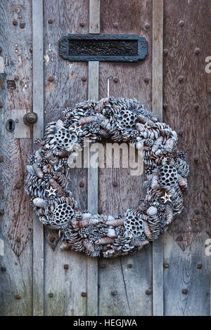 Bianco Natale corona conica sulla vecchia quercia legno chiodati porta. Stanton, Cotswolds, Inghilterra Foto Stock