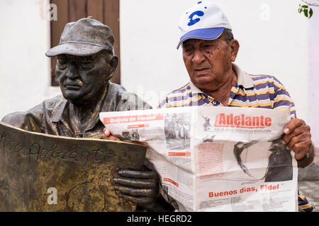 Uomo si siede la lettura di un quotidiano accanto a una scultura in bronzo di lui leggendo un giornale dall'artista Martha Jimenez, in Plaza del Carmen, Camaguey, Cuba Foto Stock