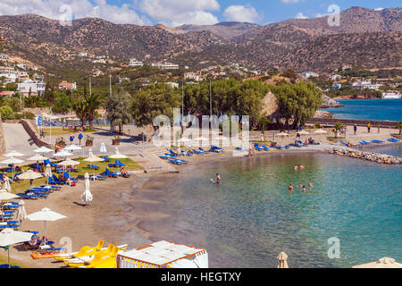 AGIOS NIKOLAOS, Grecia - 2 agosto 2012: turisti nuotare nel mare Mediterraneo sulla spiaggia di uno degli alberghi con abbondanza di sedie a sdraio e para Foto Stock