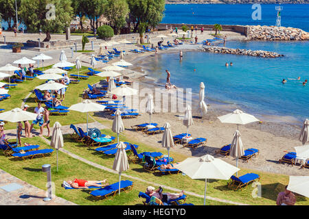 AGIOS NIKOLAOS, Grecia - 2 agosto 2012: turisti nuotare nel mare Mediterraneo sulla spiaggia di uno degli alberghi con abbondanza di sedie a sdraio e para Foto Stock