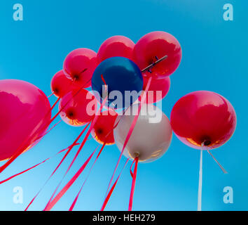 Molti palloncini colorati lanciati dai bambini felici vola nel cielo blu Foto Stock