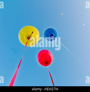Molti palloncini colorati lanciati dai bambini felici vola nel cielo blu Foto Stock