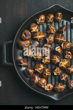 Castagne arrostite in ghisa padella per grigliare su legno scuro sfondo, vista dall'alto, composizione verticale Foto Stock