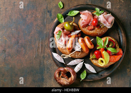 Varietà di spuntini a base di carne salsicce fritte, wienerwurst, prosciutto, marinato al peperoncino servito in salati salatini con basilico fresco su legno tagliere uovere Foto Stock