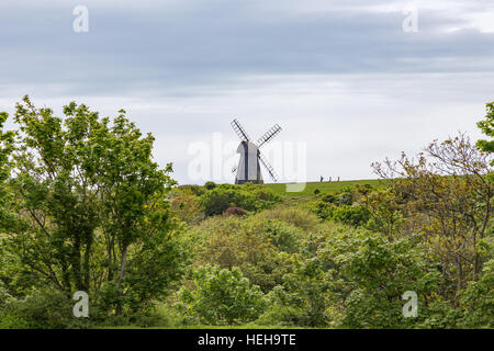 Mulino a vento sulla cima di una collina e tiro preso guardando verso l'alto. Si possono vedere tre piccoli escursionisti a piedi lungo all'orizzonte. Foto Stock