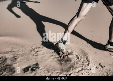 Uomo che corre attraverso la pozza di fango. Foto Stock