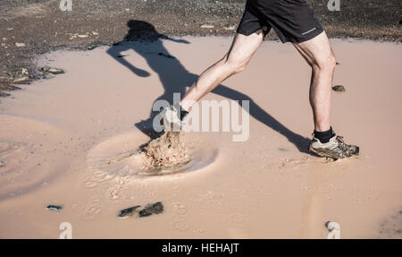 Uomo che corre attraverso la pozza di fango. Foto Stock