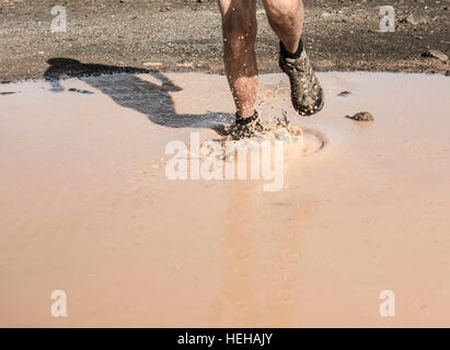 Uomo che corre attraverso la pozza di fango. Foto Stock