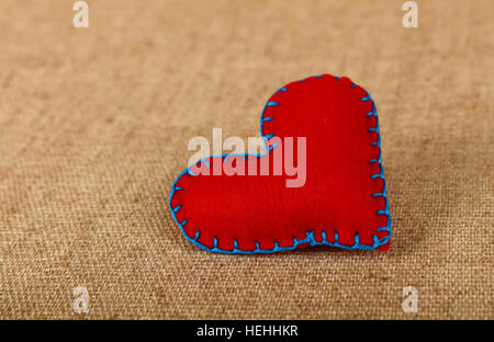 Il giorno di San Valentino modello, uno a mano feltro rosso cuciture artigianali toy cuore su tela di lino, vicino ad alto angolo di visione Foto Stock