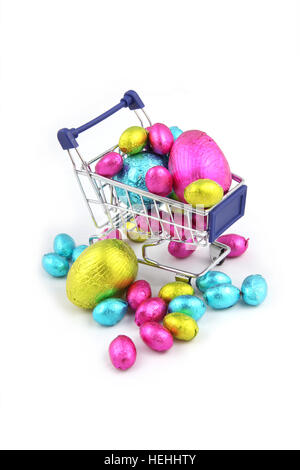 Colorate le uova di Pasqua di cioccolata in involucro di carta metallizzata, e seduto in un carrello della spesa da un super mercato su uno sfondo bianco. Foto Stock