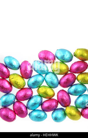 Pila di stagnola avvolto le uova di Pasqua di cioccolata in rosa, blu e verde lime con uno sfondo bianco. Foto Stock