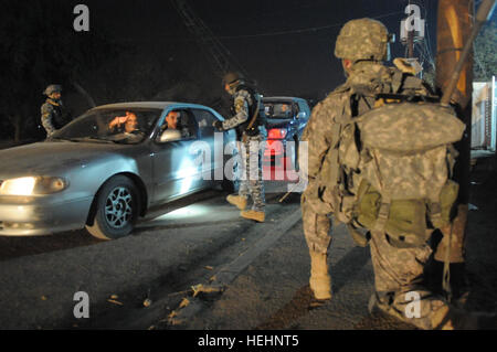 Un iracheno poliziotto nazionale del 8° Brigata, 2° Divisione trattative per gli occupanti di una vettura si è fermato a un semaforo con un punto di controllo mentre un U.S. Soldato del 2° Battaglione, 505th Parachute Reggimento di Fanteria, 3° Brigata Team di combattimento, ottantaduesima Airborne Division, fornisce la sicurezza, in Muhallah 734, Beladiyat orientale, Baghdad, Iraq, a gennaio 8, 2009. Funzionamento congiunto con la nazionale irachena di polizia sul funzionamento in avanti la fedeltà di Base 144319 Foto Stock