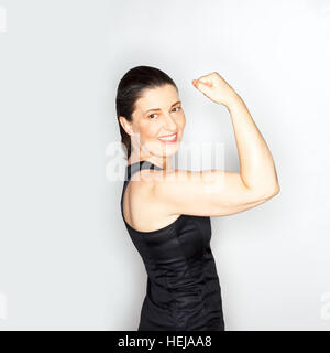 Sicuro di sé donna adulta in nero muscleshirt mostrando il suo bisceps muscoli, sfondo luminoso, sensibile design, spazio di copia Foto Stock