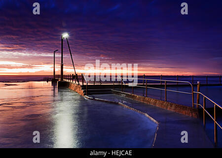 Dark Nuvoloso Tramonto su roccia piscina e spiaggia di Sydney Nord Spiagge Costa. Leadway alla piscina sotto lonely street light scollegato da alta Foto Stock