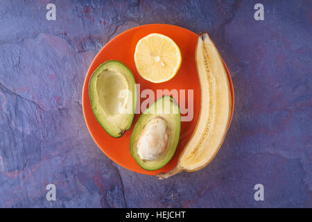 Frutti tropicali sulla piastra di colore arancione su sfondo blu orizzontale Foto Stock