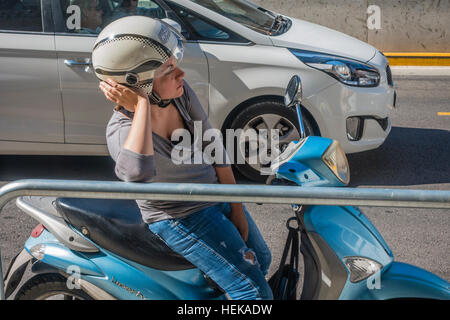 Una femmina di scooter driver bloccato nel traffico si appoggia contro una ringhiera come ella attende per il traffico per cancellare fino a Barcellona, Spagna. Foto Stock