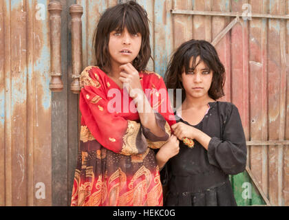 Due giovani ragazze afgane guarda con apprensione come le forze della coalizione e afghane DI POLIZIA IN UNIFORME preparare per la detonazione di un esplosivo improvvisato dispositivo vicino la loro casa nel quartiere Sharana, provincia Paktika, Afghanistan. IED è stato chiamato da un locale e situato sul lungo un frequentemente percorsa strada tra due paesani. IED stessa è stata una vittima-dispositivo attivato che non distingue tra civili o gli obiettivi militari. In attesa di espirare 482638 Foto Stock