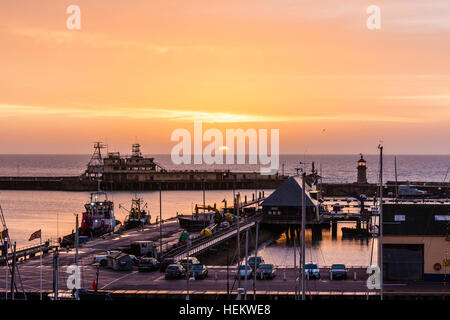 Inghilterra, Ramsgate. Alba sul Canale della Manica e il porto. Cielo arancione con nuvole. Piccolo faro alla fine del porto. Foto Stock