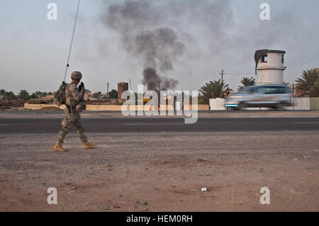 Un pennacchio di fumo nero si accumula nella distanza e velocità di auto da come Sgt. Michael Drake, un militare di poliziotti hanno assegnato alla società di sede, 2° Brigata truppe speciali Battaglione, 2° Brigata, ottantaduesima Airborne Division, passeggiate lungo una strada fuori dal Camp Taji, Iraq, durante una pattuglia smontati Dic. 2. La MPs arrotolato a lungo prima di sunrise per pattugliare le strade al di fuori del campo per garantire la sicurezza di 2/82 di convogli che viaggiano attraverso la zona da Baghdad. La seconda brigata è l'ultimo dei vigili del fuoco a Bagdad ed è facilitare il ritiro degli Stati Uniti per le forze militari da Iraq. Drake è un nativo di Virginia Beach, Foto Stock