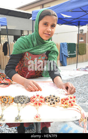 Una giovane ragazza afgana sorrisi e pone per la telecamera come ella imposta gioielli presso le donne afghane's Bazaar, nuovo composto di Kabul, Afghanistan, Ottobre 23, 2013. Le donne afghane e i bambini venuti a NKC a vendere homespun artigianato e altro ancora. Il bazar è una opportunità per le donne e i bambini per aiutare a sostenere le loro famiglie attraverso la vendita di souvenir afghano. (U.S. Foto dell'esercito da Sgt. 1. Classe Timoteo Prato, 1° Theatre supporto comando degli affari pubblici/RILASCIATO) Chitter-chatter di giovani I bambini riempiono l'aria come nuovo composto di Kabul, le donne afgane%%%%%%%%E2%%%%%%%%80%%%%%%%%99s Bazaar molle alla vita 13102 Foto Stock