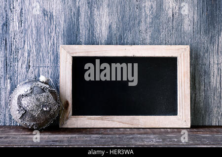 Un di legno-incorniciato lavagna con uno spazio vuoto e un elegante palla di natale su un rustico di una superficie di legno Foto Stock