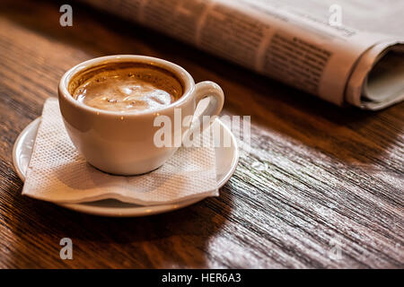 Tazza di caffè e un giornale su un tavolo di legno. Buona mattina o pausa caffè concetto. Foto Stock