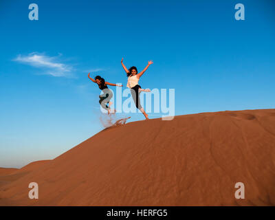 Due giovani donne che salta da dune di sabbia nel deserto, Sharqiya sabbie o Wahiba Sands, Al Raka, Oman Foto Stock