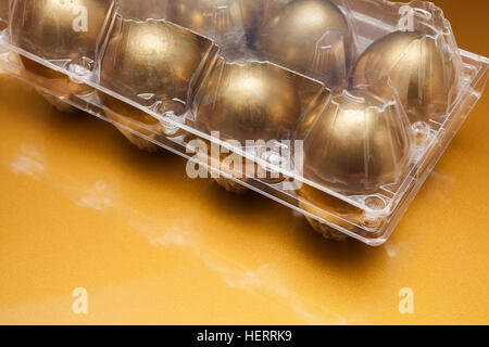 Golden uova in una scatola di plastica su sfondo dorato Foto Stock