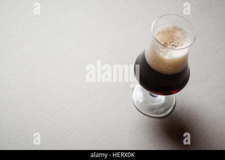 Tulip bicchiere pieno di dark Birra stout su una tabella di colore grigio Foto Stock