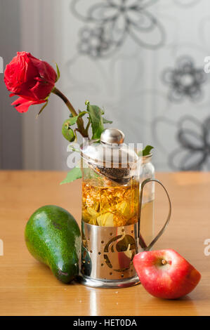 Teiera con press, una rosa rossa, un avocado, un pezzo di Apple sul tavolo di legno Foto Stock