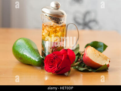 Teiera con press, una rosa rossa, un avocado, un pezzo di Apple sul tavolo di legno Foto Stock