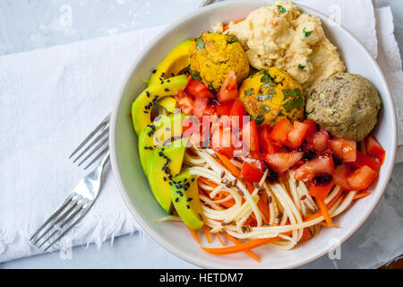 Zucchine, carote spaghetti con sfere vegana, avocado e hummus. Vista dall'alto sul cemento grigio Sfondo. Cibo Vegan concetto. Foto Stock
