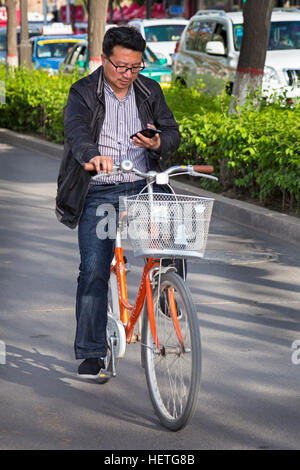 Ciclista cinese utilizzando il suo telefono cellulare, Yinchuan, Ningxia, Cina Foto Stock