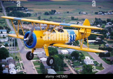 Un giallo pozzetto aperto biplano Stearman vola basso su di una piccola città del Midwest. Foto Stock