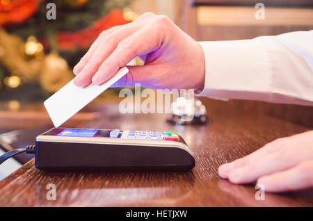 Maschio caucasico in maglia bianca pagando bill contactless con carta di credito. Foto Stock