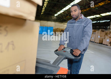 Lavoratore di magazzino utilizzando il carrello per movimentazione pallet Foto Stock