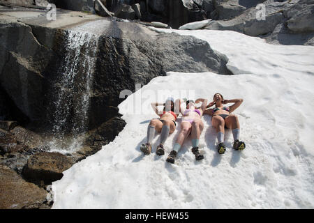 Tre giovani donne che indossano bikini, giacente in neve il incantesimi, Alpine Lakes Wilderness, Washington, Stati Uniti d'America Foto Stock