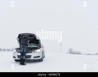 Vista posteriore dell'uomo guardando sotto il cofano di ripartiti auto su paesaggi innevati Foto Stock