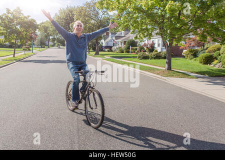 Senior uomo con le mani alzate mentre escursioni in bicicletta lungo la strada suburbana Foto Stock