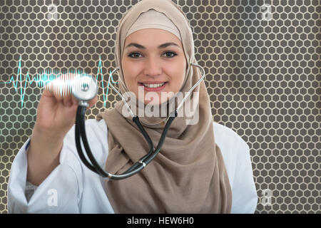 Close up ritratto di donna araba medico sorridere mentre utilizzando uno stetoscopio Foto Stock