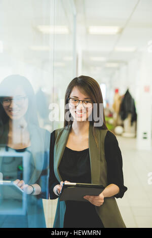 Ritratto di giovane donna appoggiata contro office porta utilizzando tavoletta digitale Foto Stock