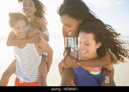 Giovane uomo e donna piggybacking amici sulla spiaggia, Cape Town, Sud Africa Foto Stock