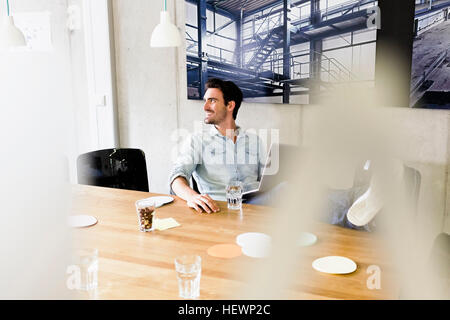 Business man in office piedi sulla scrivania, utilizzando laptop che guarda lontano sorridente Foto Stock
