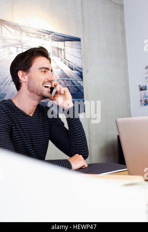 Uomo in ufficio utilizzando il telefono cellulare, che guarda lontano sorridente Foto Stock