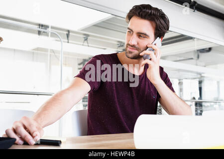 Uomo in ufficio utilizzando il telefono cellulare, che guarda lontano Foto Stock