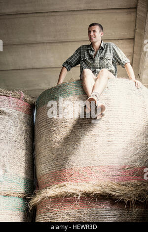 Ritratto di giovane maschio farmworker sulla sommità del pagliaio in Fattoria Barn Foto Stock