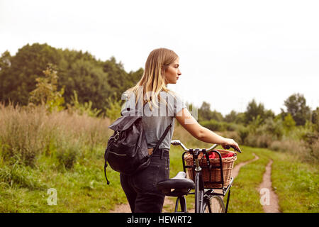 Giovane donna con la bicicletta guardando sopra la sua spalla da rurale traccia di sporco Foto Stock
