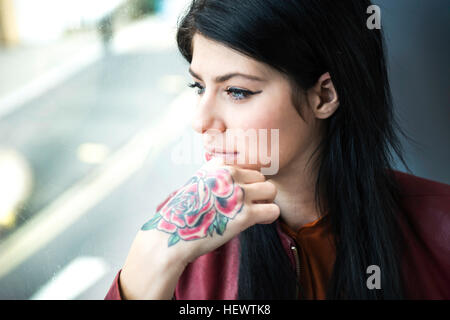 Giovane donna con il tatuaggio sul lato, guardando attraverso la finestra Foto Stock