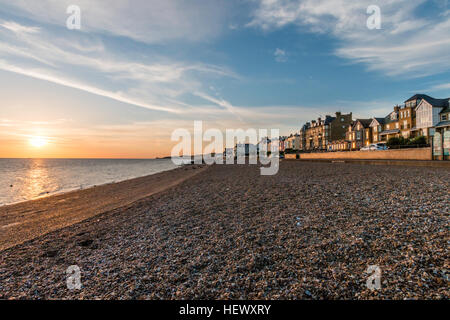 Vista lungo la spiaggia di ciottoli con la passeggiata sul lungomare e la città durante il tramonto sul mare. In distanza, capezzagna a Reculver. Foto Stock