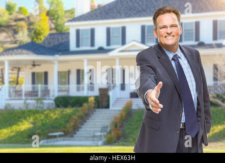 Sorridente agente maschile raggiungendo per agitare a mano nella parte anteriore della bella casa di nuova costruzione. Foto Stock